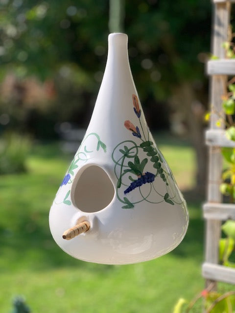 A white ceramic bird feeder with hand-painted floral and vine designs in green, blue, and pink.
