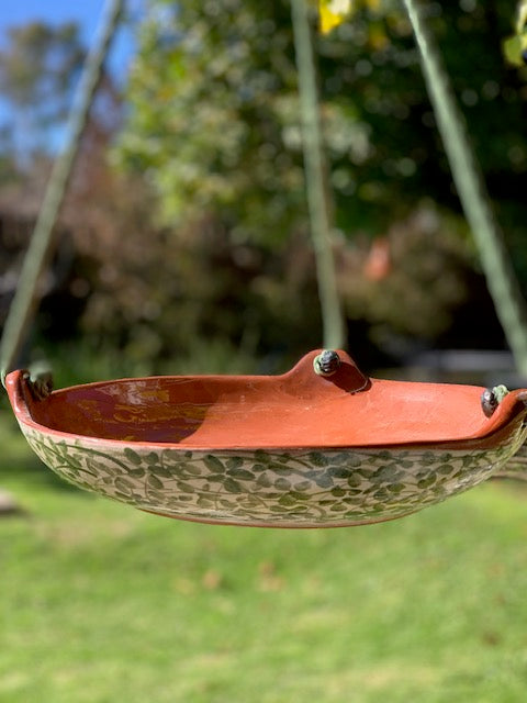 A handmade ceramic  garden tray, suspended by green ropes in an outdoor garden setting.